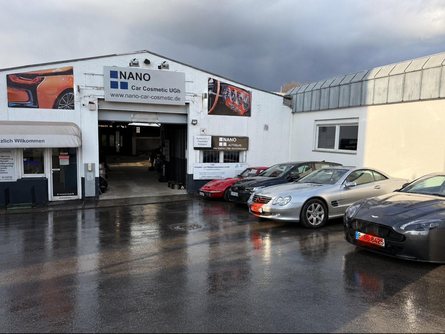 Werkstatteingang von Nano Car Cosmetic mit klassischen Fahrzeugen bei Tageslicht