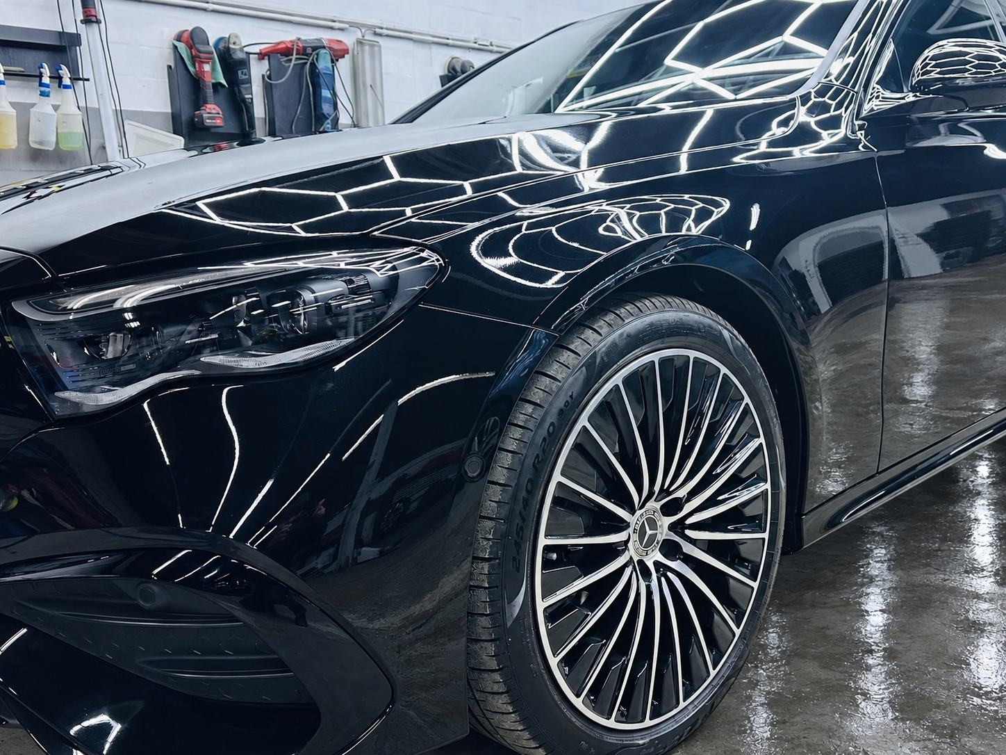 Schwarzer Mercedes mit Mehrspeichenfelge und Spiegelungen der Werkstattbeleuchtung – Werkstattboden digital bearbeitet.