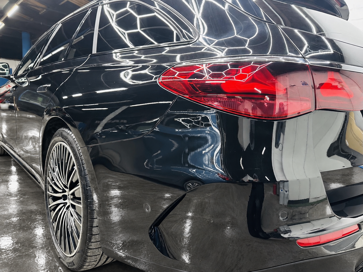 Schwarzer Mercedes in seitlicher Heckansicht mit roter Rückleuchte und glänzender Lackoberfläche – Werkstattboden digital bearbeitet.