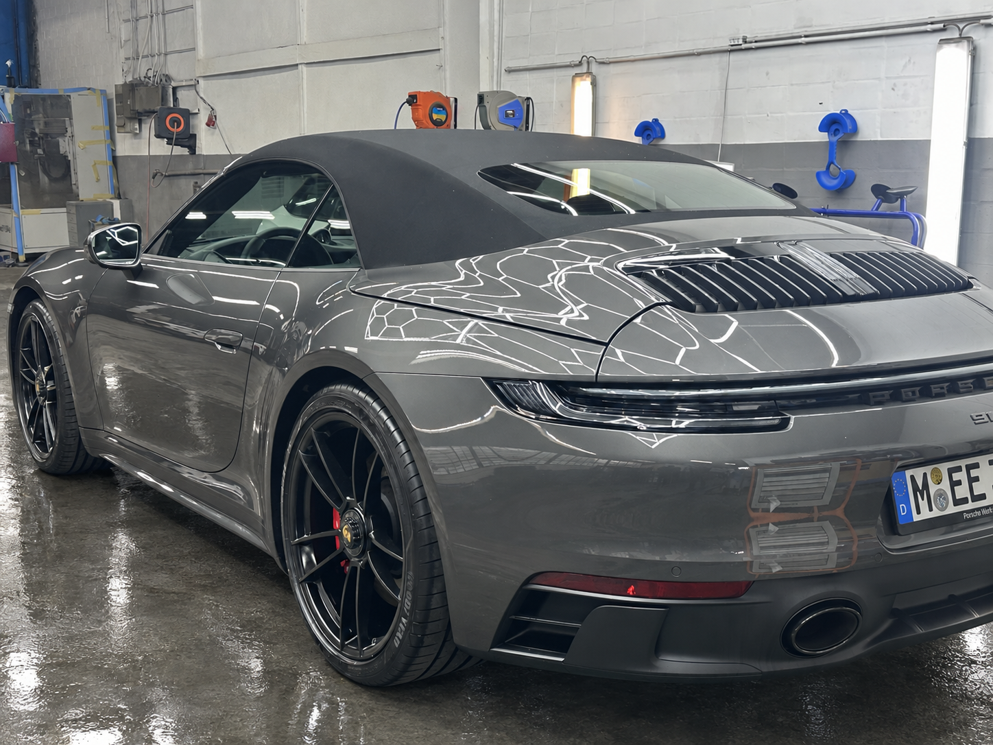 Graues Porsche-Cabrio mit geschlossenem Stoffverdeck und schwarzen Felgen in der Werkstatt – Werkstattboden digital bearbeitet.