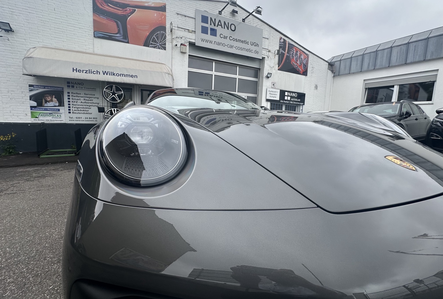 Graue Porsche-Front mit rundem Scheinwerfer vor der Werkstattfassade von Nano Car Cosmetic