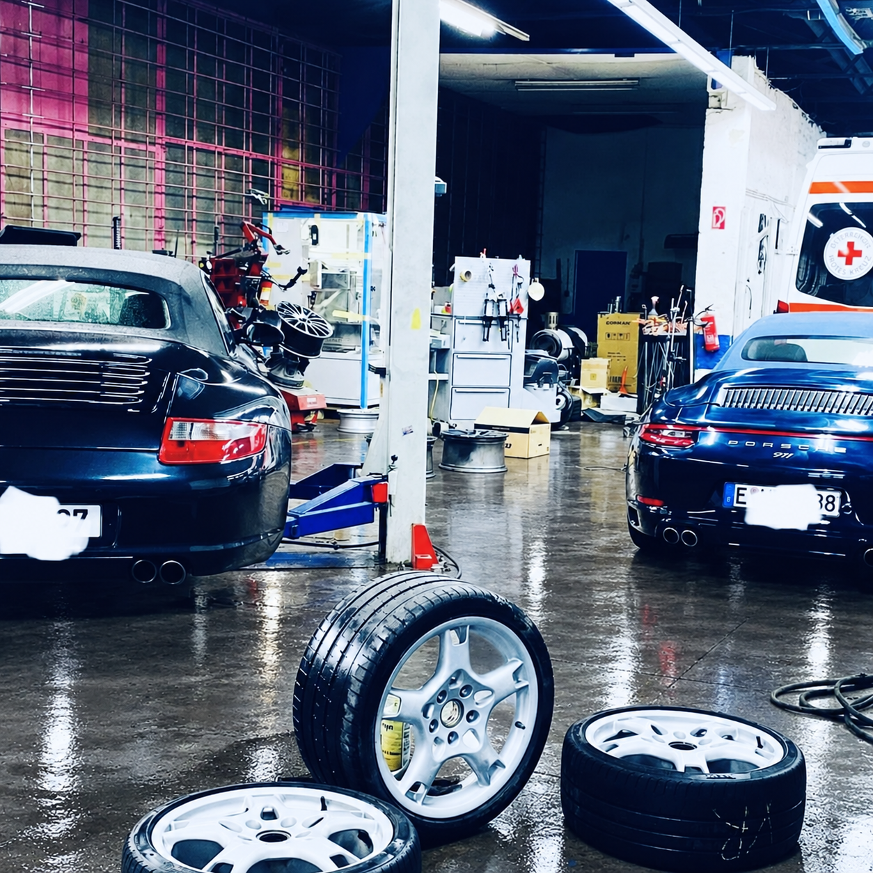 Zwei Porsche in der Werkstatt mit demontierten Rädern im Vordergrund – Werkstattboden digital bearbeitet.