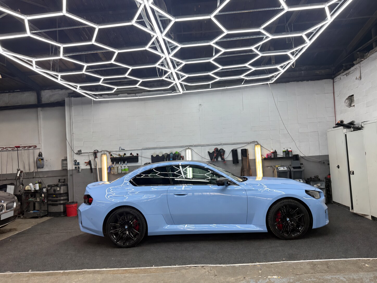 Hellblaues BMW-Coupé in der Seitenansicht mit Spiegelungen der Werkstattbeleuchtung